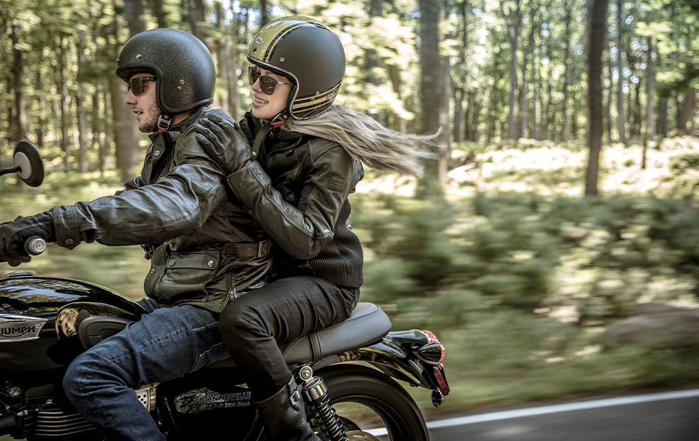 Homem e mulher em cima da moto com floresta em volta